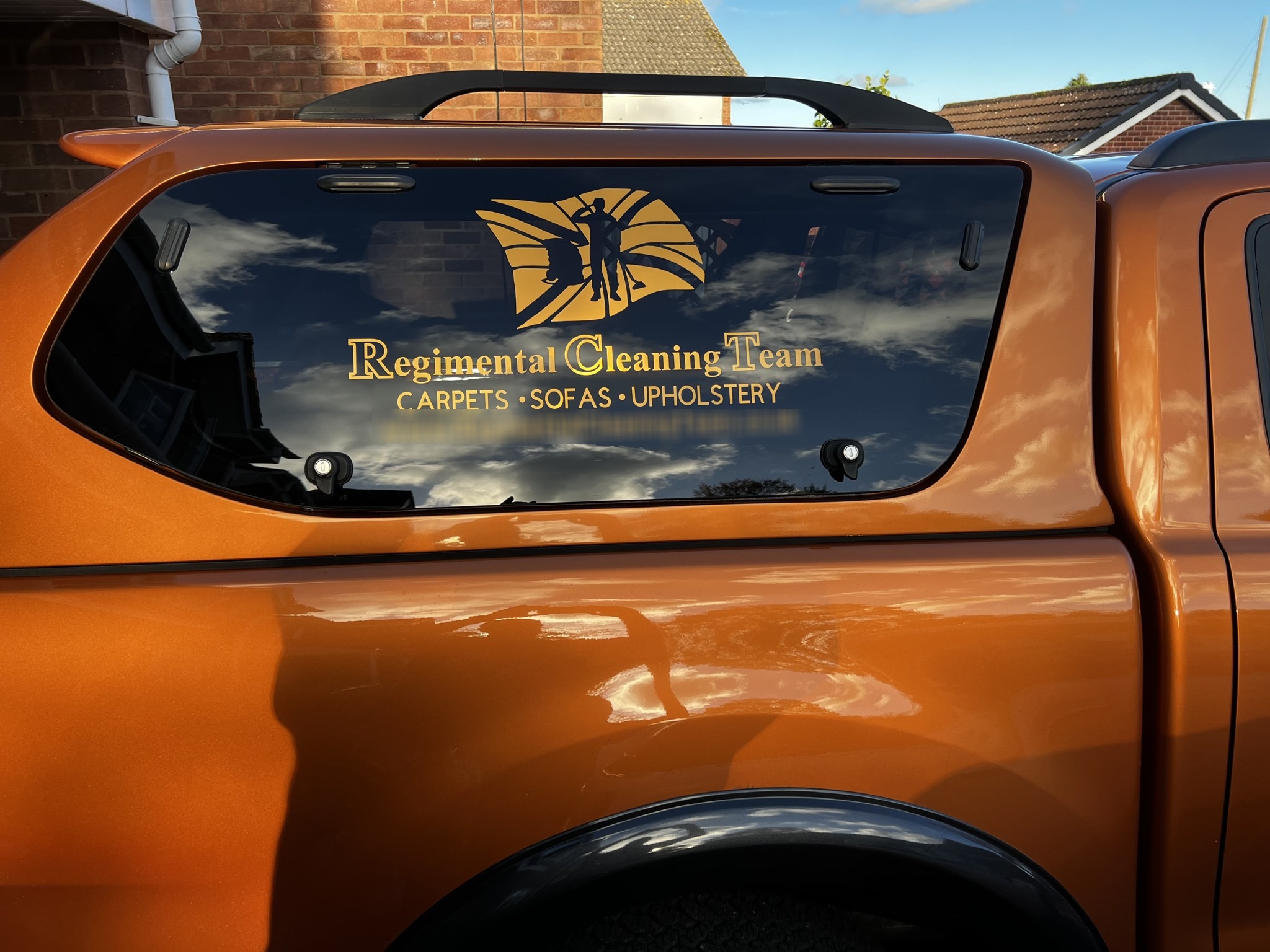 Orange pickup truck with the Regimental Cleaning Team flag logo on its canopy window